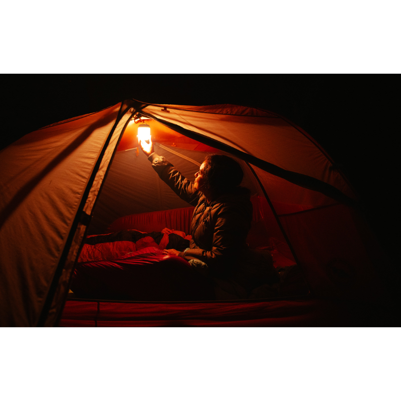 A woman holding a Alpenglow 250 Lantern inside her camping tent. 