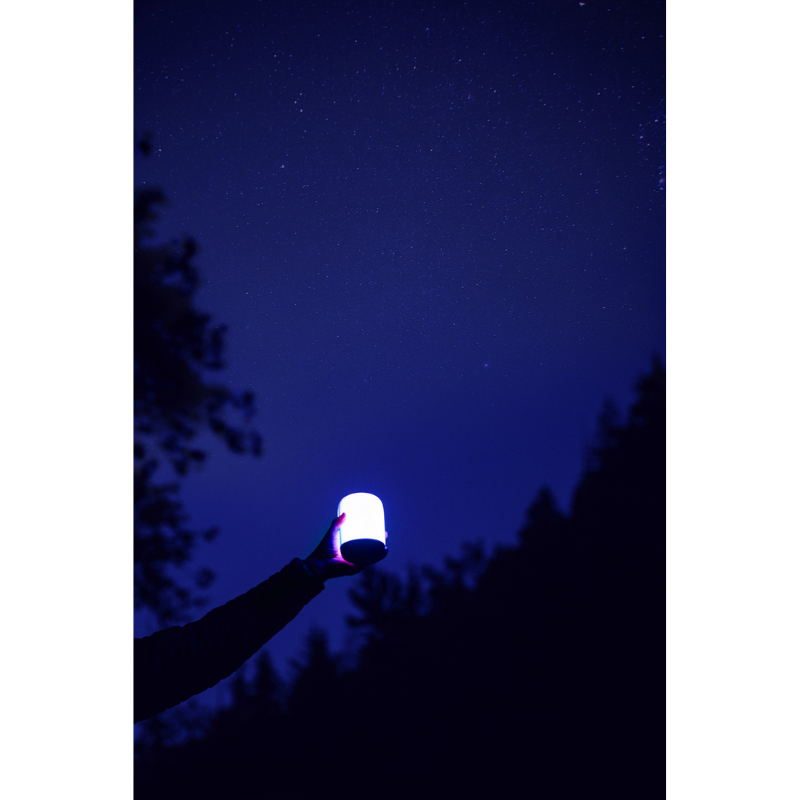 A person holding a Alpenglow 250 Lantern out in the night. 