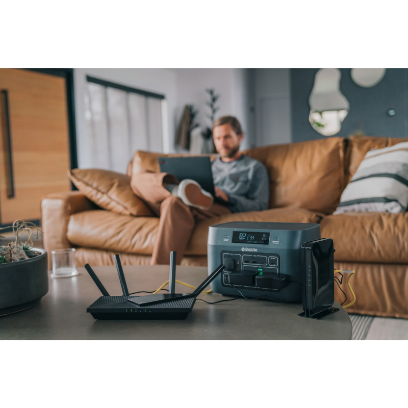 Image of a man on a couch using his laptop while the modem is plugged in on BaseCharge 600.